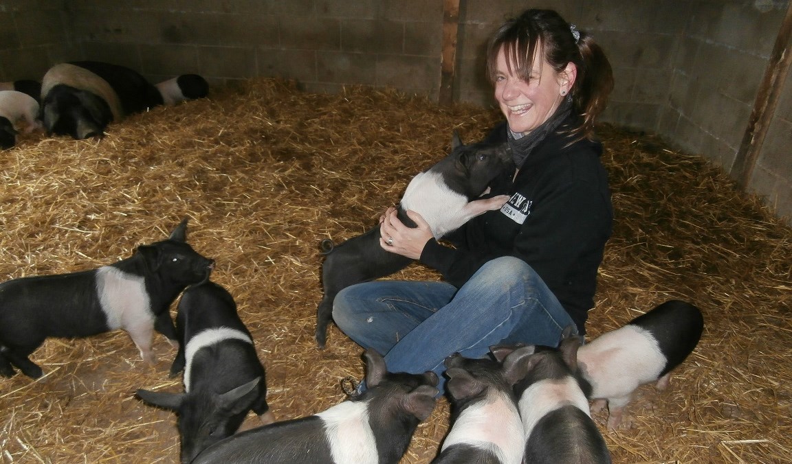 lady sat in straw bedding surrounded by piglets